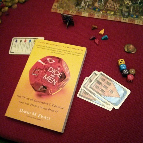 The book “Of Dice and Men” on a red table clothes. Next to it some
cards, dice and token and the boardgame
Bruges